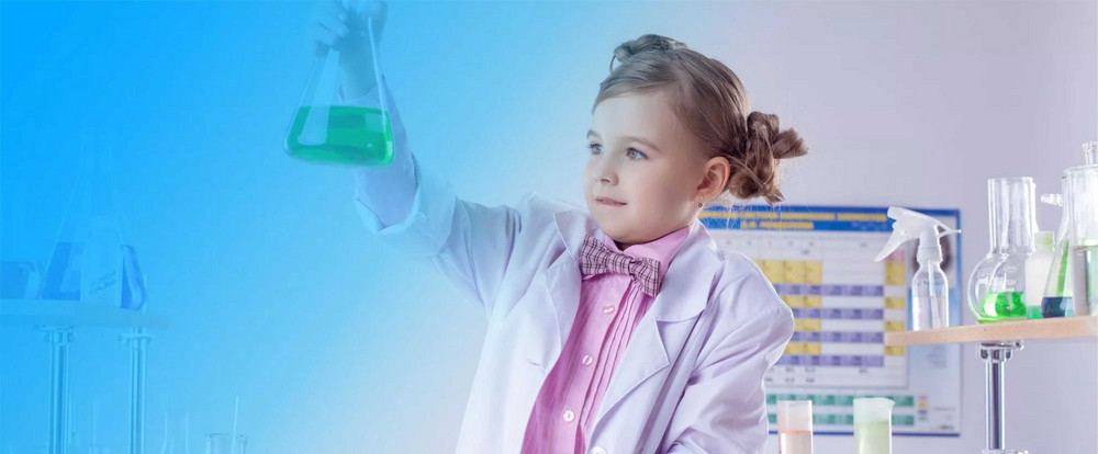 Dziewczynka w białym fartuchu. Trzyma szkła laboratoryjne.