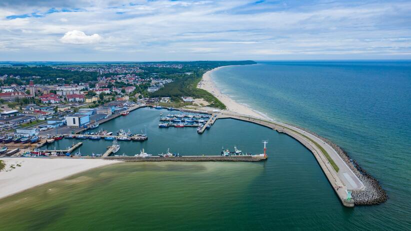 Widok na port morski położony nad otwartym morzem, którego część stanowi zachodni falochron pełniący także funkcję turystycznego mola.