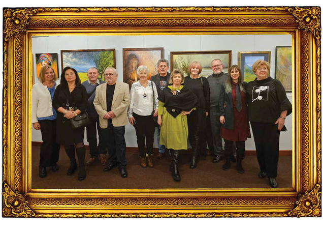 Zdjęcie grupy artystów podczas wernisażu w złoconej, zdobionej ramce